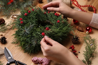 Florist making beautiful Christmas wreath with berries at wooden table, closeup