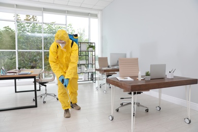 Photo of Janitor in protective suit disinfecting office to prevent spreading of COVID-19