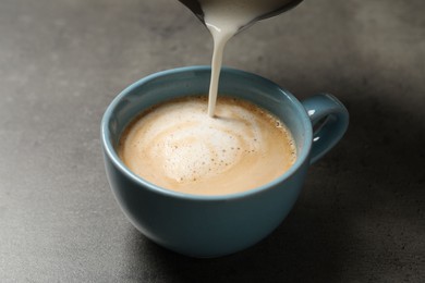 Photo of Pouring milk into cup of coffee on grey table, closeup