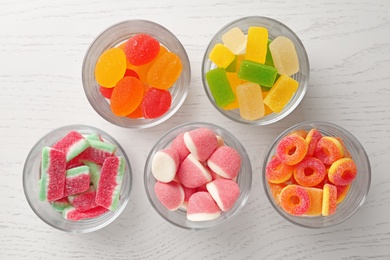 Glass bowls of different jelly candies on white wooden table, flat lay