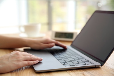 Woman working with modern laptop at wooden table, closeup