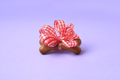 Photo of Bone shaped dog cookie with red bow on purple background