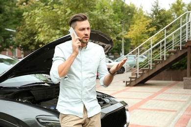 Photo of Man talking on phone near broken car outdoors