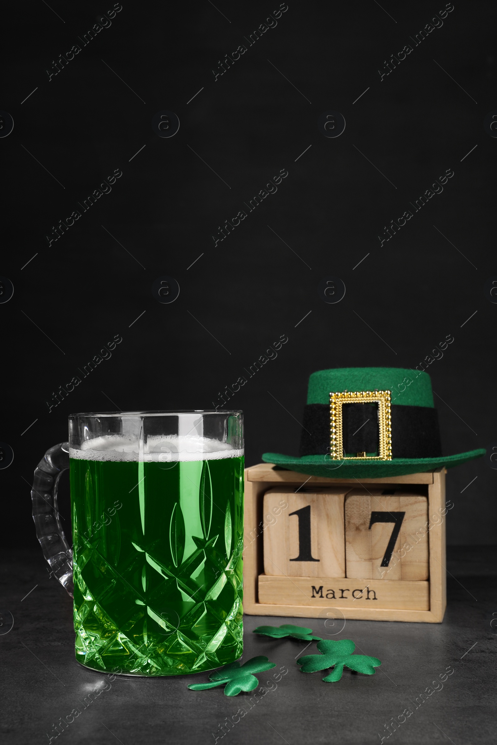 Photo of St. Patrick's day celebrating on March 17. Green beer, wooden block calendar, leprechaun hat and decorative clover leaves on grey table. Space for text