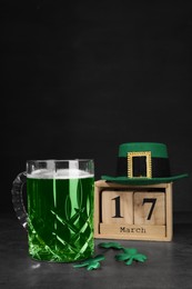 St. Patrick's day celebrating on March 17. Green beer, wooden block calendar, leprechaun hat and decorative clover leaves on grey table. Space for text