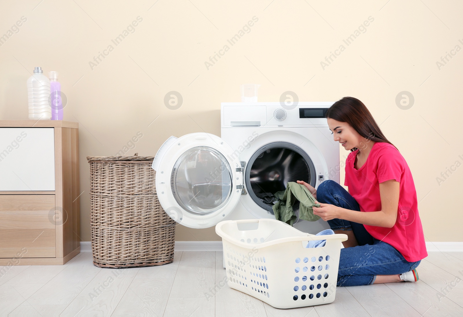 Photo of Young woman taking laundry out of washing machine at home