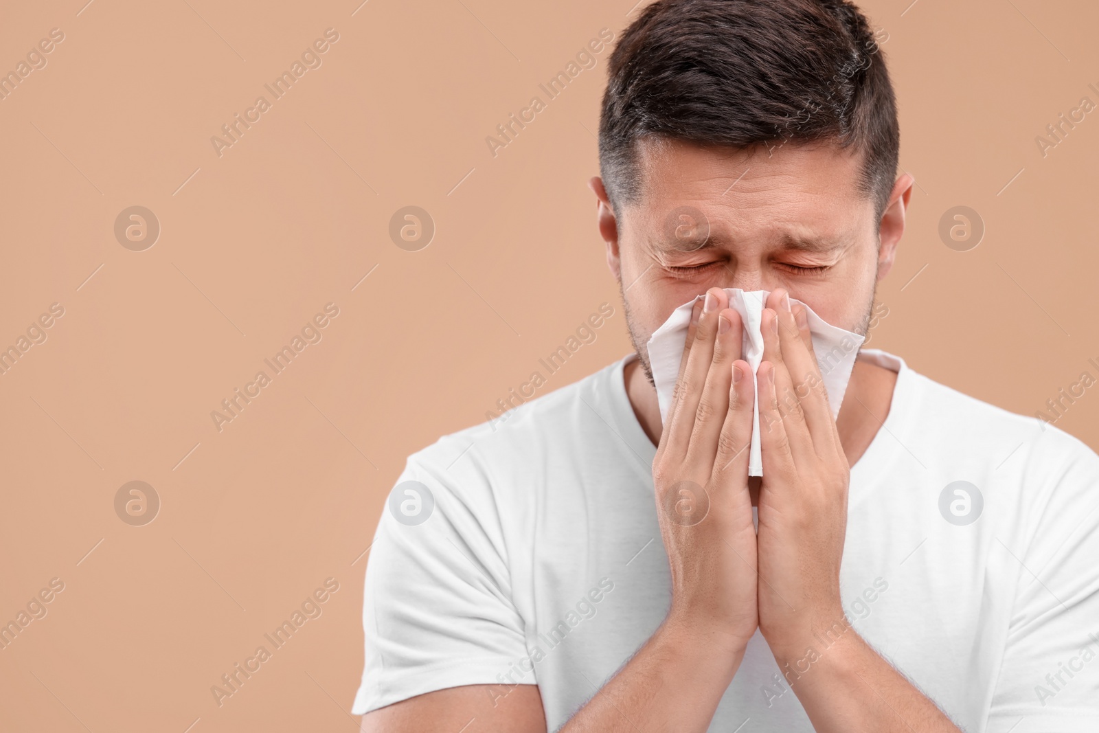 Photo of Allergy symptom. Man sneezing on light brown background. Space for text