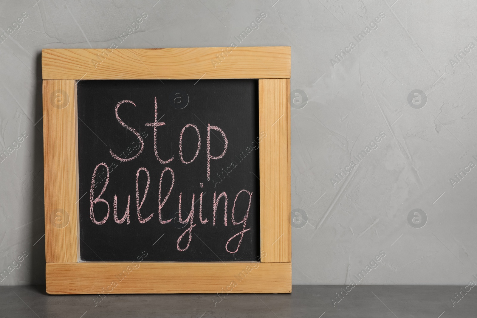 Photo of Blackboard with phrase Stop Bullying on table near grey wall
