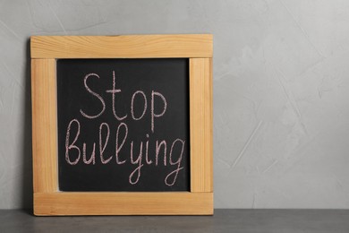 Blackboard with phrase Stop Bullying on table near grey wall