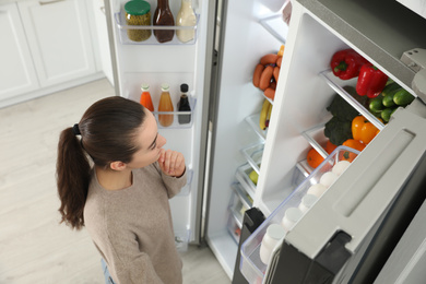Photo of Young woman near open refrigerator indoors, above view