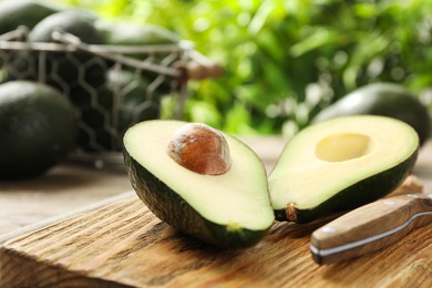 Halves of delicious ripe avocado on wooden board against blurred background