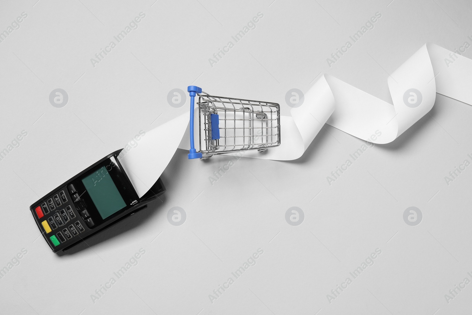 Photo of Payment terminal with thermal paper for receipt and small shopping cart on light grey background, flat lay