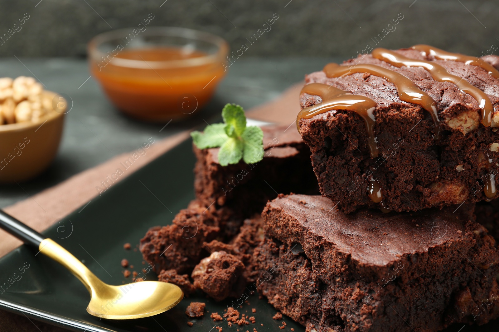 Photo of Delicious chocolate brownies with nuts, caramel sauce and fresh mint on plate, closeup