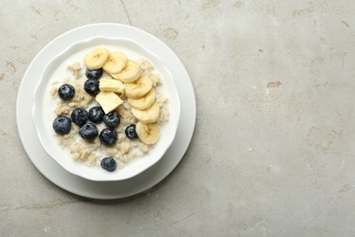 Tasty oatmeal with banana, blueberries, butter and milk served in bowl on light grey table, top view. Space for text