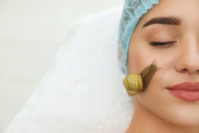 Young woman receiving snail facial massage in spa salon. Space for text