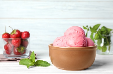 Photo of Bowl with delicious strawberry ice cream on white wooden table against light background