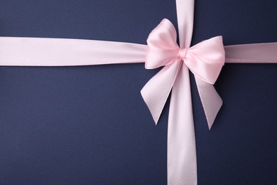 Photo of Pink satin ribbon with bow on blue background, top view