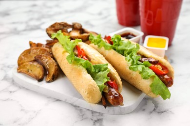 Photo of Tasty hot dogs with potato wedges served on white marble table, closeup. Fast food