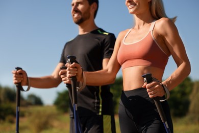 Photo of Couple practicing Nordic walking with poles outdoors on sunny day, selective focus