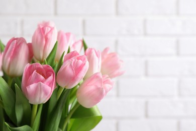 Beautiful bouquet of tulips against white brick wall, closeup. Space for text