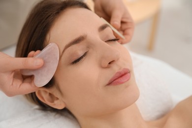 Young woman receiving facial massage with gua sha tools in beauty salon, closeup