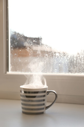 Cup of hot drink near window on rainy day. Space for text