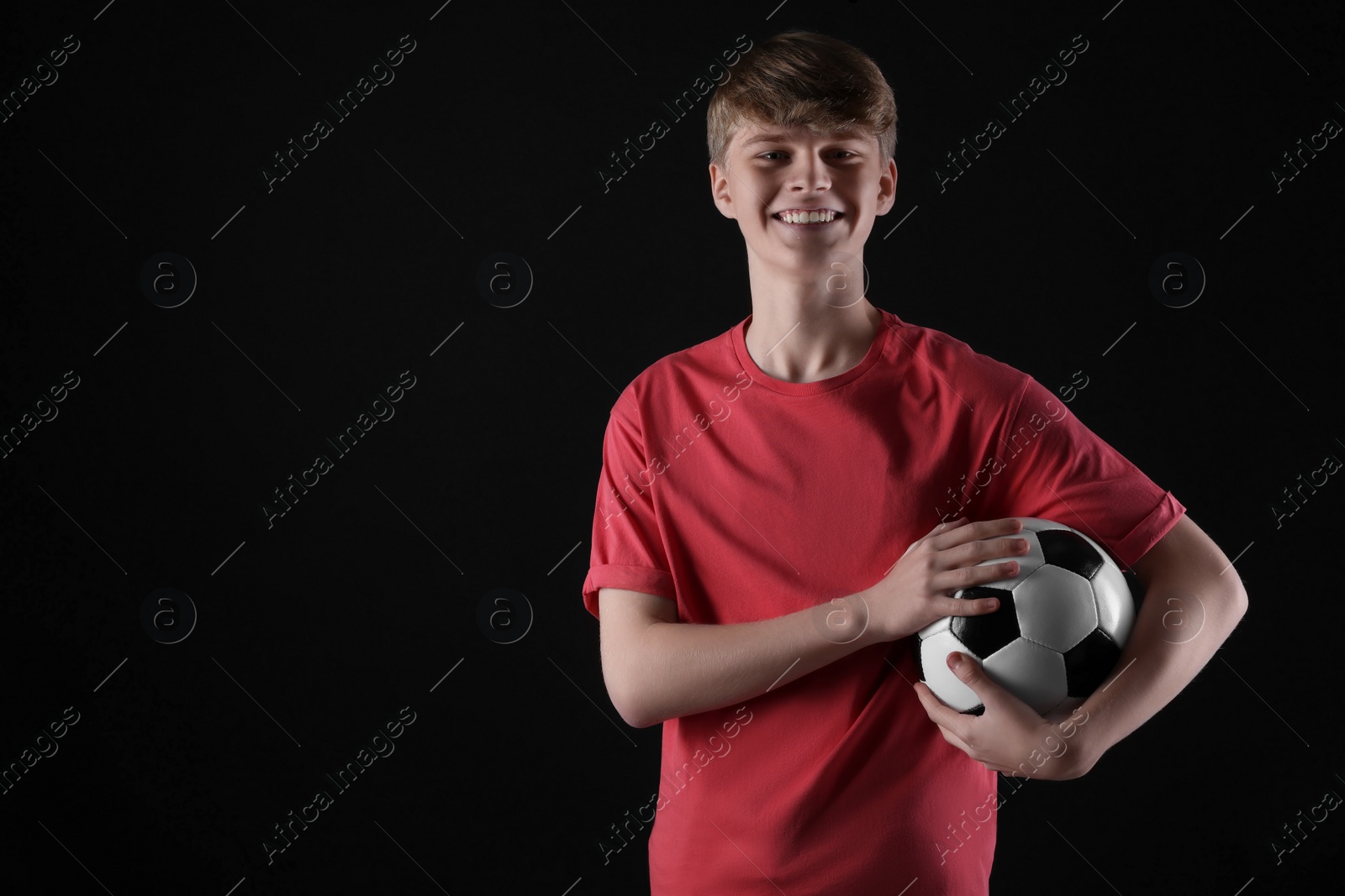 Photo of Teenage boy with soccer ball on black background. Space for text