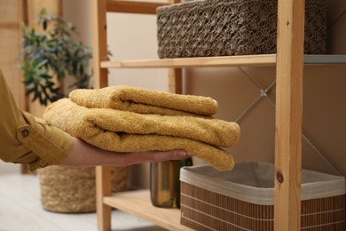 Photo of Woman putting towels into storage basket indoors, closeup