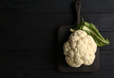 Photo of Fresh raw cauliflower on black wooden table, top view. Space for text