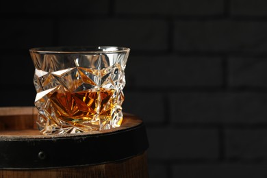 Photo of Glass of tasty whiskey on wooden barrel, closeup. Space for text