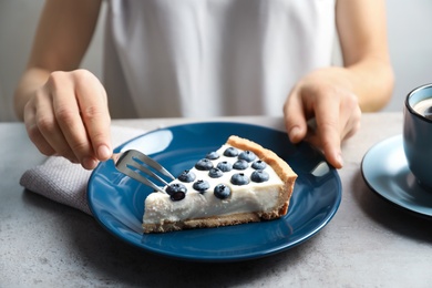 Woman eating tasty blueberry cake at table, closeup