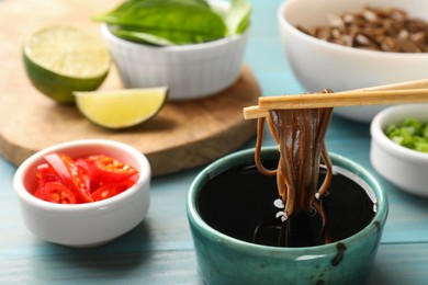 Photo of Eating delicious buckwheat noodles (soba) with chopsticks at light blue wooden table, closeup