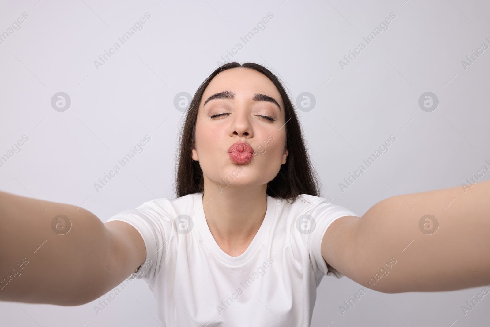 Photo of Young woman taking selfie and blowing kiss on white background