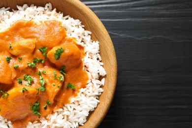 Photo of Bowl of butter chicken with rice on wooden background, top view. Space for text