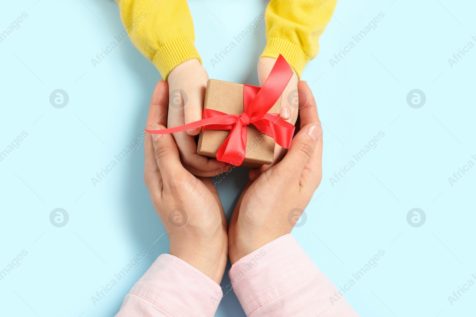 Photo of Mother giving gift box to her child on light blue background, top view