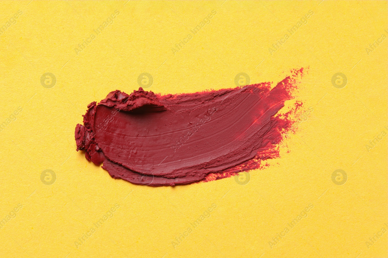 Photo of Smear of bright lipstick on yellow background, top view