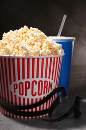 Photo of Delicious popcorn, drink and tape on grey table