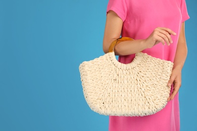 Photo of Young woman with stylish straw bag on light blue background, closeup. Space for text