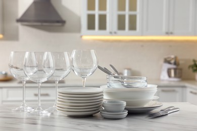 Photo of Different clean dishware, cutlery and glasses on white marble table in kitchen