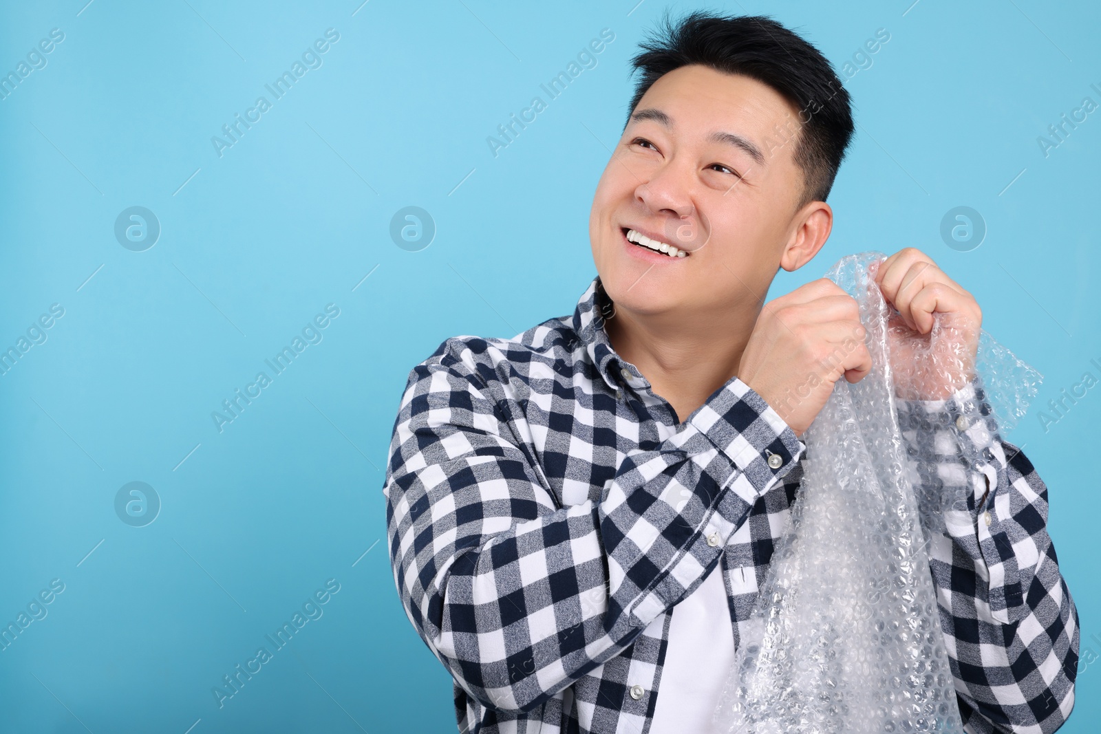 Photo of Happy asian man with bubble wrap on light blue background. Space for text