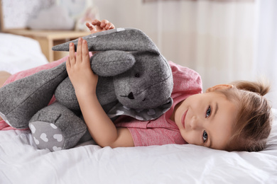 Cute little girl with toy bunny on bed at home