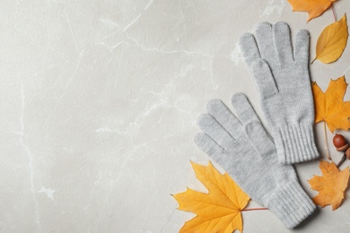 Stylish gloves and dry leaves on light grey table, flat lay. Space for text