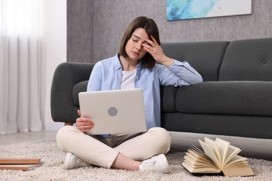 Overwhelmed woman with laptop sitting on floor indoors