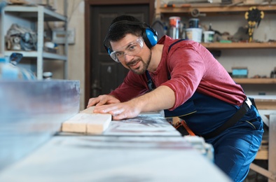 Photo of Mature man using wood working machine at carpentry shop