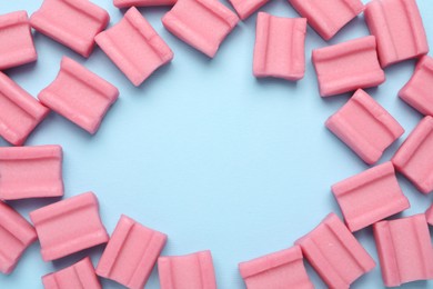 Photo of Frame of tasty pink chewing gums on light blue background, flat lay. Space for text