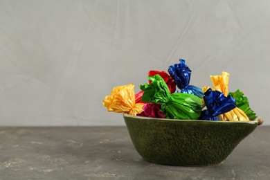 Photo of Candies in colorful wrappers on grey table, space for text