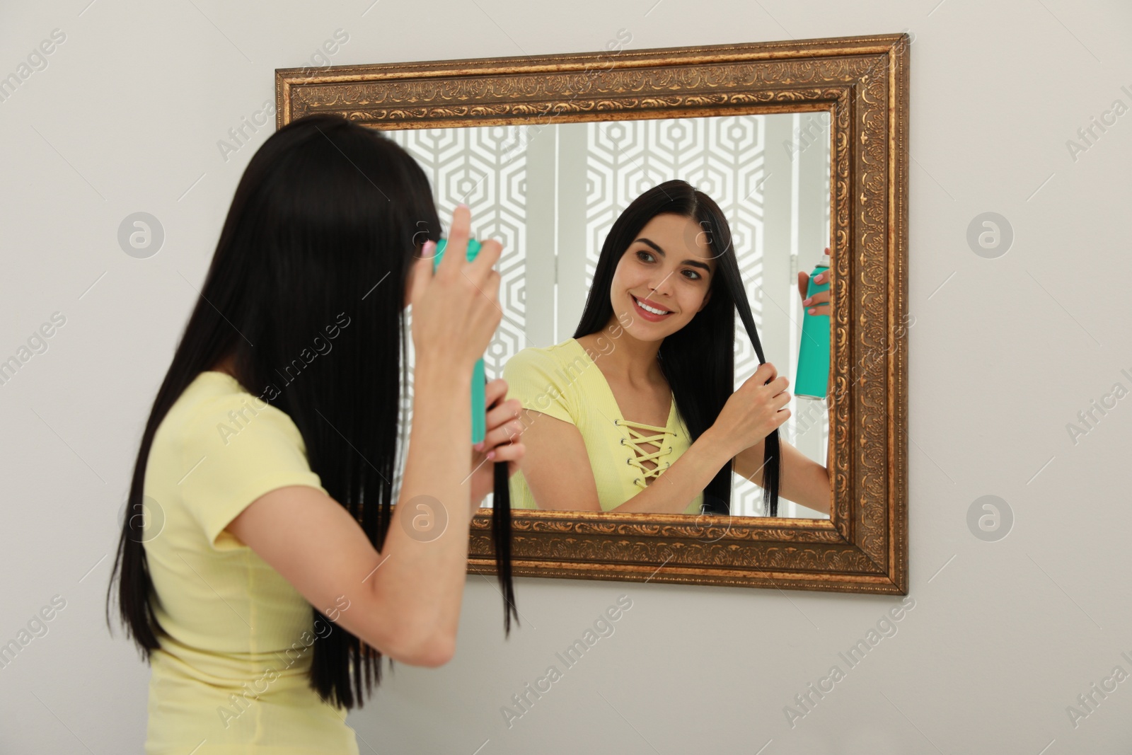 Photo of Woman applying dry shampoo onto her hair near mirror