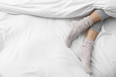 Woman wearing warm socks in comfortable bed, above view. Space for text