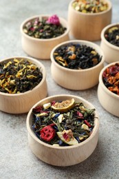 Photo of Different kinds of dry herbal tea in wooden bowls on light grey table