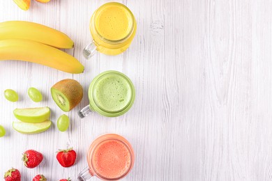 Photo of Many different tasty smoothies and ingredients on white wooden table, flat lay. Space for text